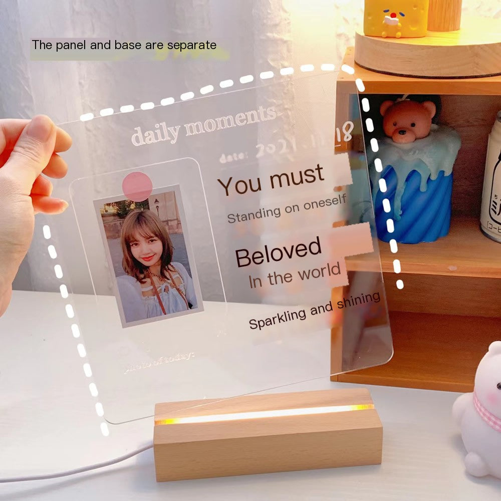Transparent photo frame with wooden base on a desk with a teddy bear and other items.