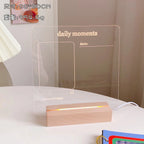 Transparent acrylic board with 'daily moments' text and wooden base on a white surface.