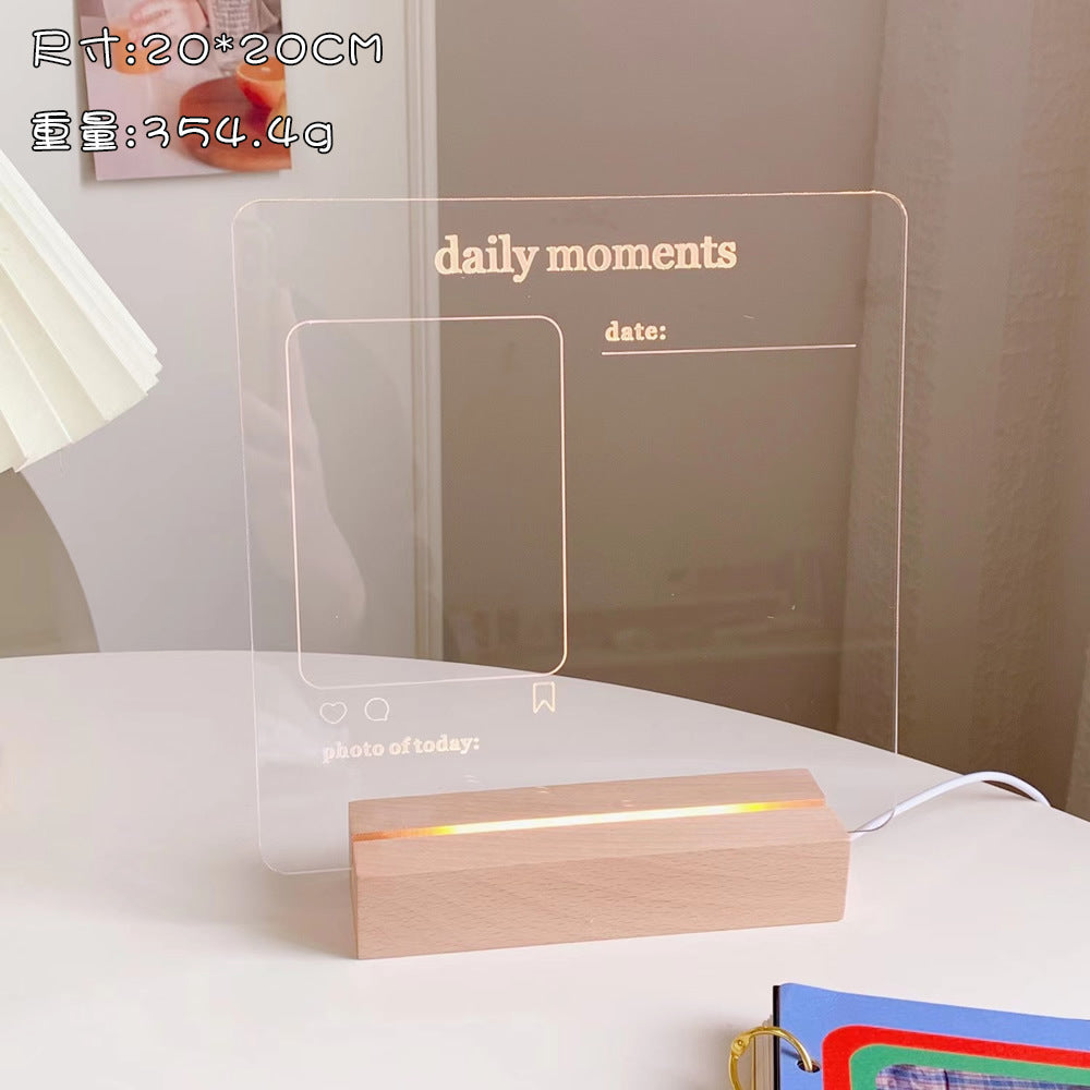 Transparent acrylic board with 'daily moments' text and wooden base on a white surface.